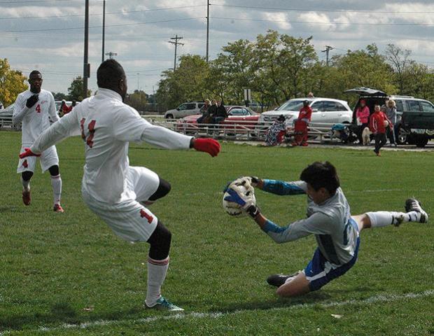 Ancilla's Rene Mejia makes a save as Glenroy Miller of the Express looks to score in the first half of today's 1-0 upset win for Ancilla. Photo by Nicholas Huenefeld/Owens Sports Information